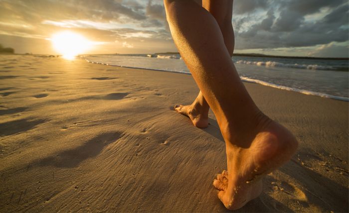 bare feet walking on beach during sunset